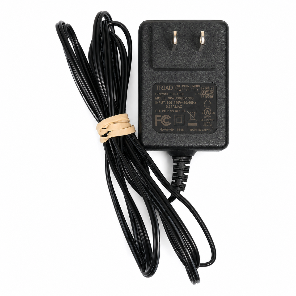 A black TRIAD brand power adapter with a coiled black cable secured by a beige rubber band, shown on a plain white background.